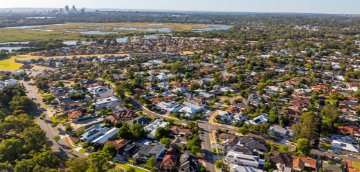 Image of an aerial view of suburban homes beside wetlands, with a distant city skyline.